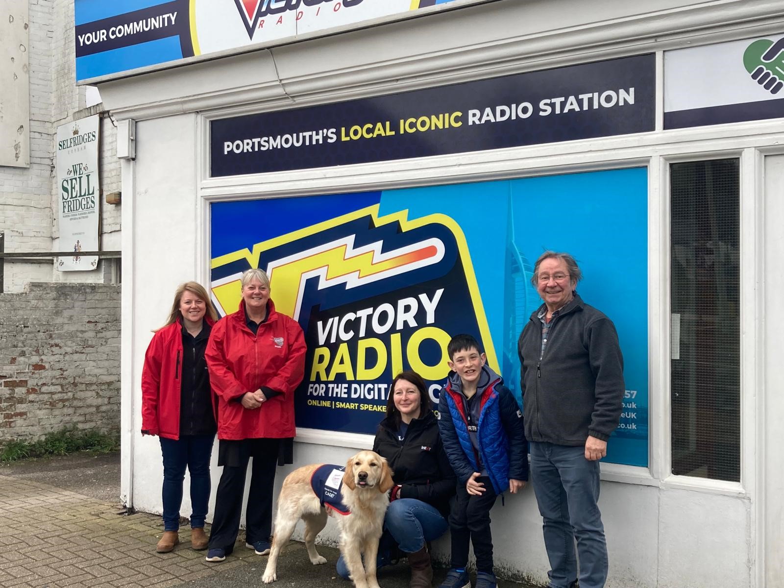 Five people including one child &amp; a Golden Retriever in an assistance dog jacket outside Victory Radio HQ