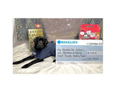 Black Labrador laying down on a robe next to a cheque for £1028.70