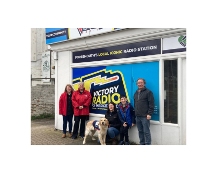 Group shot of 5 people & an assistance dog in training outside Victory Radio