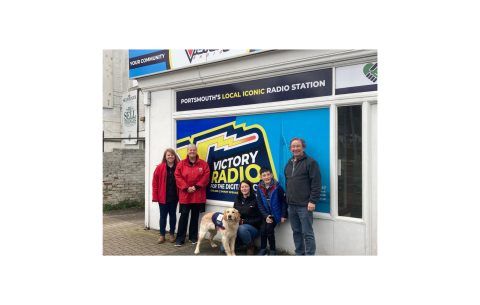 Group shot of 5 people & an assistance dog in training outside Victory Radio