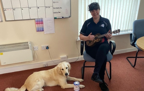 Hounds for Heroes dog trainer habituating a dog in training with a ukulele