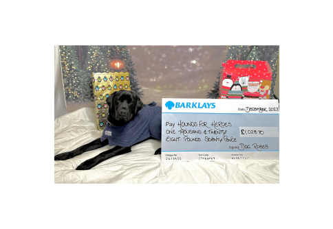 Black Labrador laying down on a robe next to a cheque for £1028.70